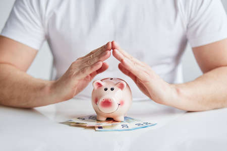 Man makes the roof from hands over pink piggy bankの写真素材