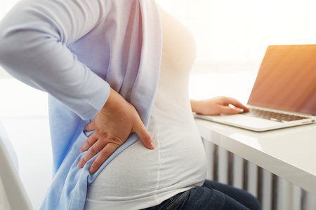 Pregnant woman in the office has back painの写真素材