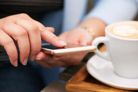 Woman using a mobile phone near a cappuccino cup