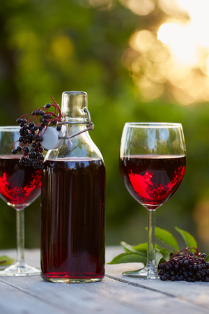 Glasses of elderberry wine and elderberries on wooden tableの写真素材