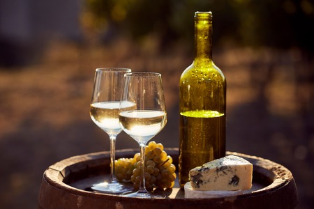 Two glasses of white wine and bottle with food at sunsetの写真素材