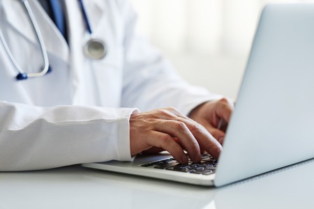 Male doctor working on laptop at clinicの写真素材