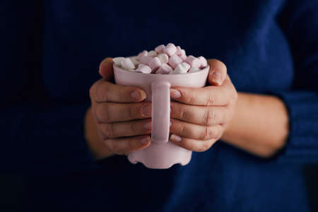 Female hands with pink mug of hot chocolate and marshmallow