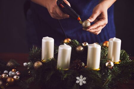 Florist sticking christmas ball with hot gun on wreathの写真素材