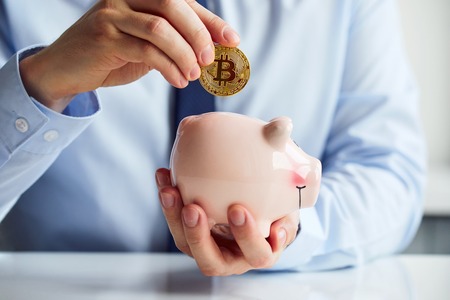 Man putting Bitcoin into piggy bank in the officeの写真素材