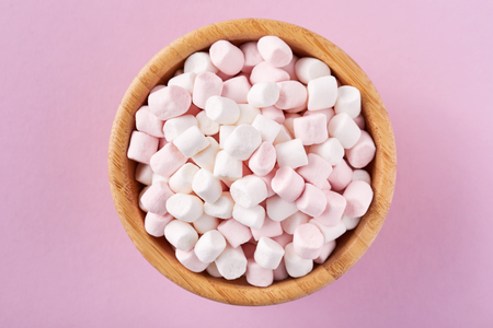 White and pink marshmallows in wooden bowl on pink background, top viewの写真素材