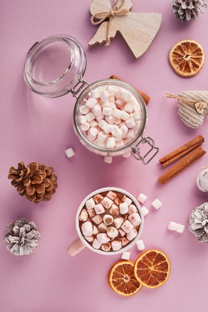 View from above at marshmallows in mug, glass jar and Christmas decoration on pink backgroundの写真素材