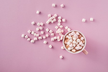Top view of white and pink marshmallows in mug on pink background
