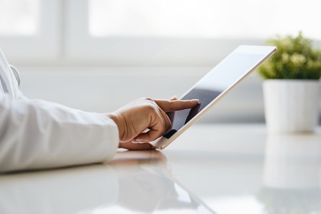 Female doctor uses tablet while sitting in medical officeの写真素材
