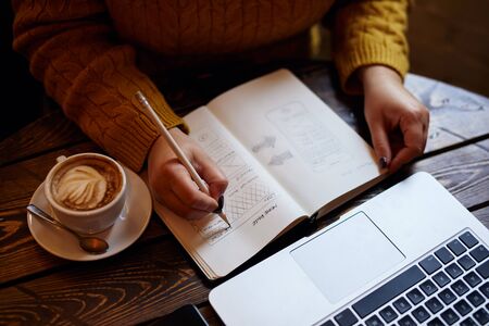 Woman sketching web design into diary in cafeの写真素材