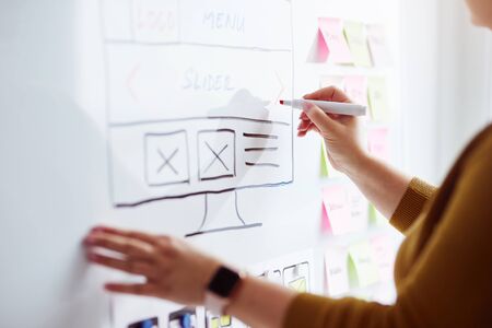 Female web designer drawing sketch of website with red marker pen on whiteboardの写真素材