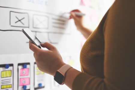 Web designer with mobile phone and marker drawing sketch of website on whiteboardの写真素材