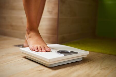 Woman weighing herself on weight scale in bathroomの写真素材