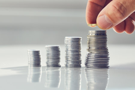 A man's hand placing a coin on a money stack, saving or investing moneyの写真素材