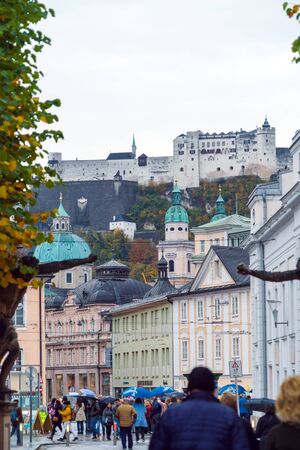 Salzburg, Austria - October 21, 2017: Tourists and locals walk through the streets of the old city in the rain against the backdrop of the Hohensalzburg castleのeditorial素材