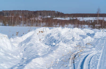 Huge piles of snow after the work of a tractor to clear rural roads in winter the consequences of heavy snowfallの写真素材