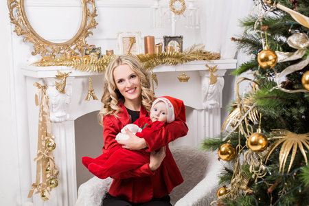 mother holding a baby in a christmas decorated room with a christmas tree and a fireplaceの写真素材