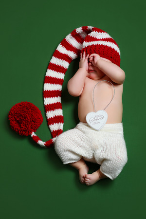cute joyful christmas baby in a red and white gnome long-tailed hat covering face with handsの写真素材
