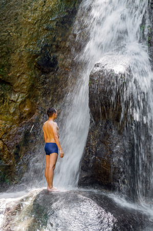 Young man standing with her hands on the stone at the waterfallの写真素材