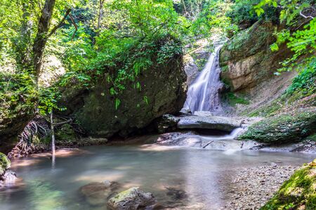 Waterfall from a cliff in the mountains. Cascade on the river. Stones covered with moss in the lake with clear water. Water in Motion. Republic of Adygea, Southern Russia.の写真素材