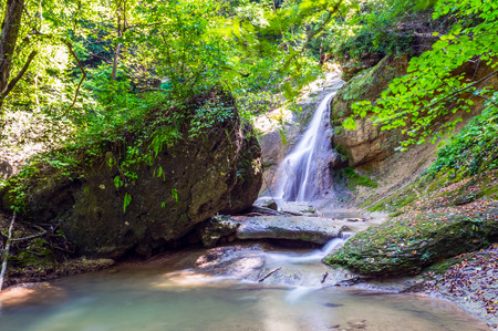 Waterfall from a cliff in the mountains. Cascade on the river. Stones covered with moss in the lake with clear water. Water in Motion. Republic of Adygea, Southern Russia.の写真素材