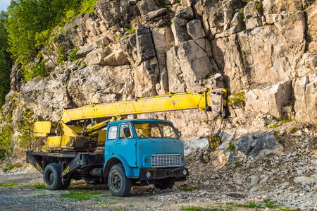 Old yellow automobile crane with blue cab and telescopic boom in transport position near with rocky mountainの写真素材