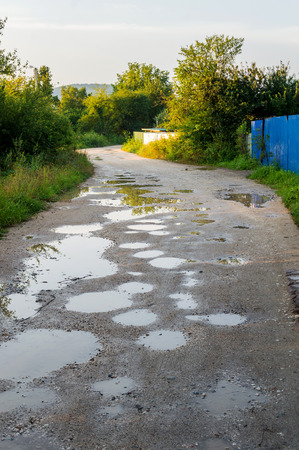 Bad Ground Road after Rain. Puddle on way. Pot hole or pothole image with a dirty water puddle as a transportation symbol of road maintenance and car insurance risk to auto suspensions.の写真素材