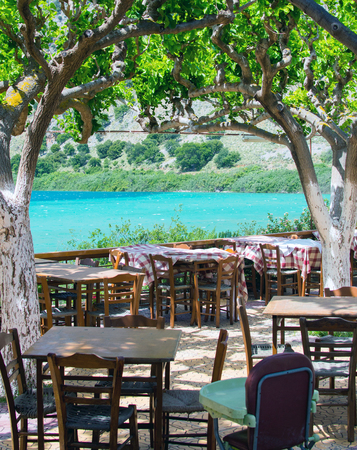Cafe tables and chairs on the shore of the lake in shadow of treesの写真素材