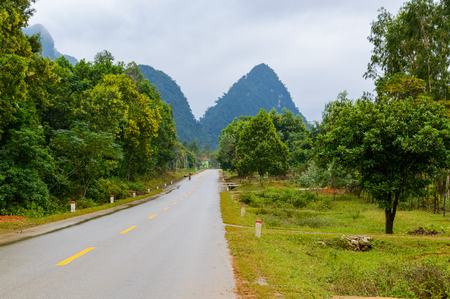 Asphalt Road in mountain area with yellow line in the middle of the road for road background or business concept. Thunder clouds in the sky.の写真素材