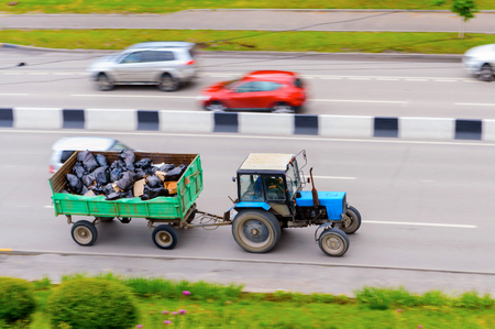 Blue tractor with trailer in motion on the road street of the cityの写真素材