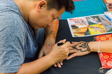 Thailand, Phuket, February 03, 2017: Asian mehendi artist. A handsome man drawing mehendi on the handのeditorial素材