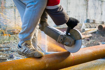 Male hand cuts off pieces of water pipe with angle grinder.の写真素材