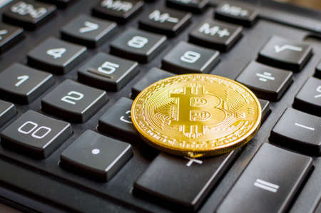 golden bitcoin coin on black calculator close up.の写真素材