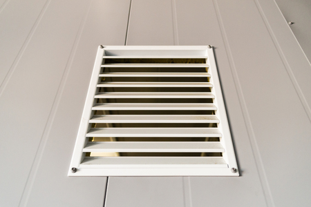 Ventilation grate on metal wall painted in grey.