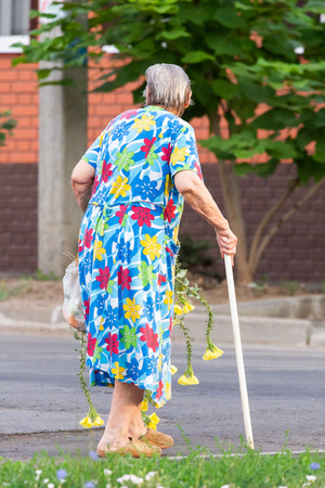 Elderly woman with flowers walking on a street.の写真素材