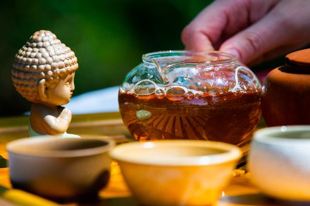 On the table on a wooden tray a teapot with tea, teapot, cups. Man, hands pouring tea.の写真素材