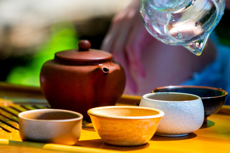 On the table on a wooden tray a teapot with tea, teapot, cups. Man, hands pouring tea.