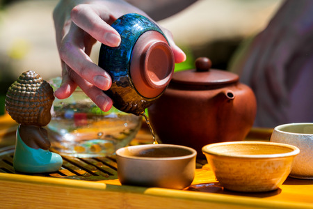 On the table on a wooden tray a teapot with tea, teapot, cups. Man, hands pouring tea.の写真素材