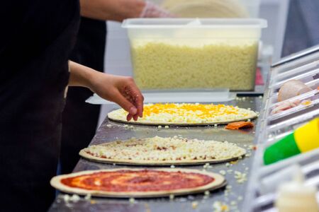 Cook in the kitchen putting the ingredients on the pizza. Pizza concept. Production and delivery of...