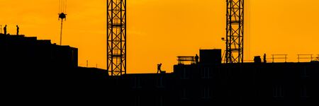 Background of silhouette building crane lift loads with sun set rays yellow cloudy evening sky backdrop Construction site at orange sunset.の写真素材