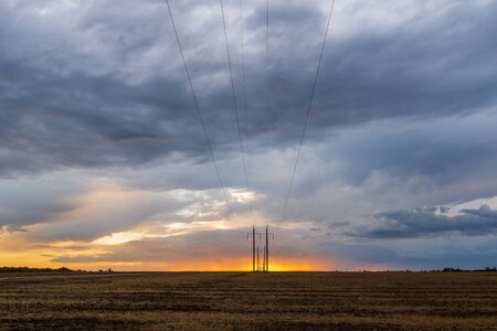 A row of high voltage electrical power lines cling to the horizon in an otherwise vast, wide open rural landscape on sunset with clouds.の写真素材