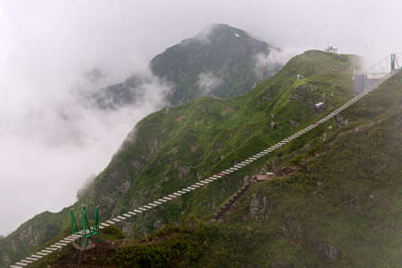 Hanging bridge over chasm in fog. Rope bridge between peaks in cloud.の写真素材