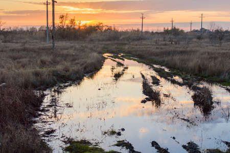 Reflection of the setting sun in a puddle on a dirt road in the Russian field.の写真素材