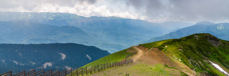 Landscape of green valley, forested mountains and a bit of snow on a grass.