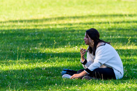 Portugal, Lisbon, October 09, 2018: Young woman use smartphone seating on grass in a park.