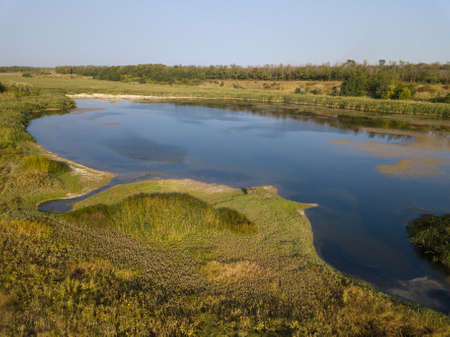 Aerial view of the countryside and a circular lake in the middle of the forest.