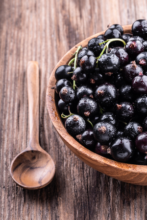 Half of big wooden bowl with fresh black currant and spoon on wooden background close-up top view . Healthy food, harvesting, vitamin, detox, vegan, vegetarian, alternative medicine.の写真素材
