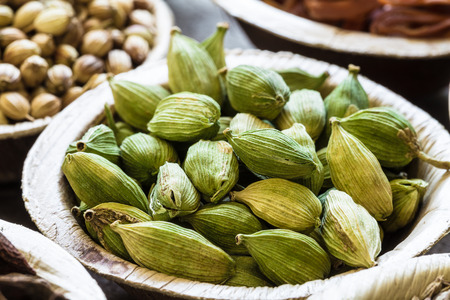 Green cardamom in coconut bowl close-up. Indian spice.