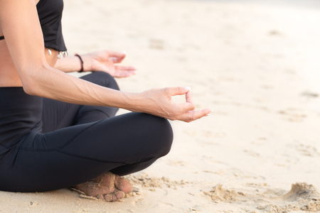 Slim strong mature woman in black practicing yoga on sand beach meditation pose close-up with copy spaceの写真素材