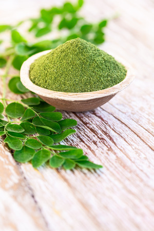 Moringa powder (Moringa Oleifera) in coconut bowl with original fresh Moringa leaves on wooden background. Healthy product, superfood, vitamin.の写真素材
